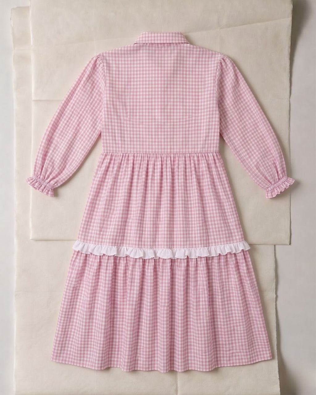 Pink gingham dress with white lace trim on a beige background