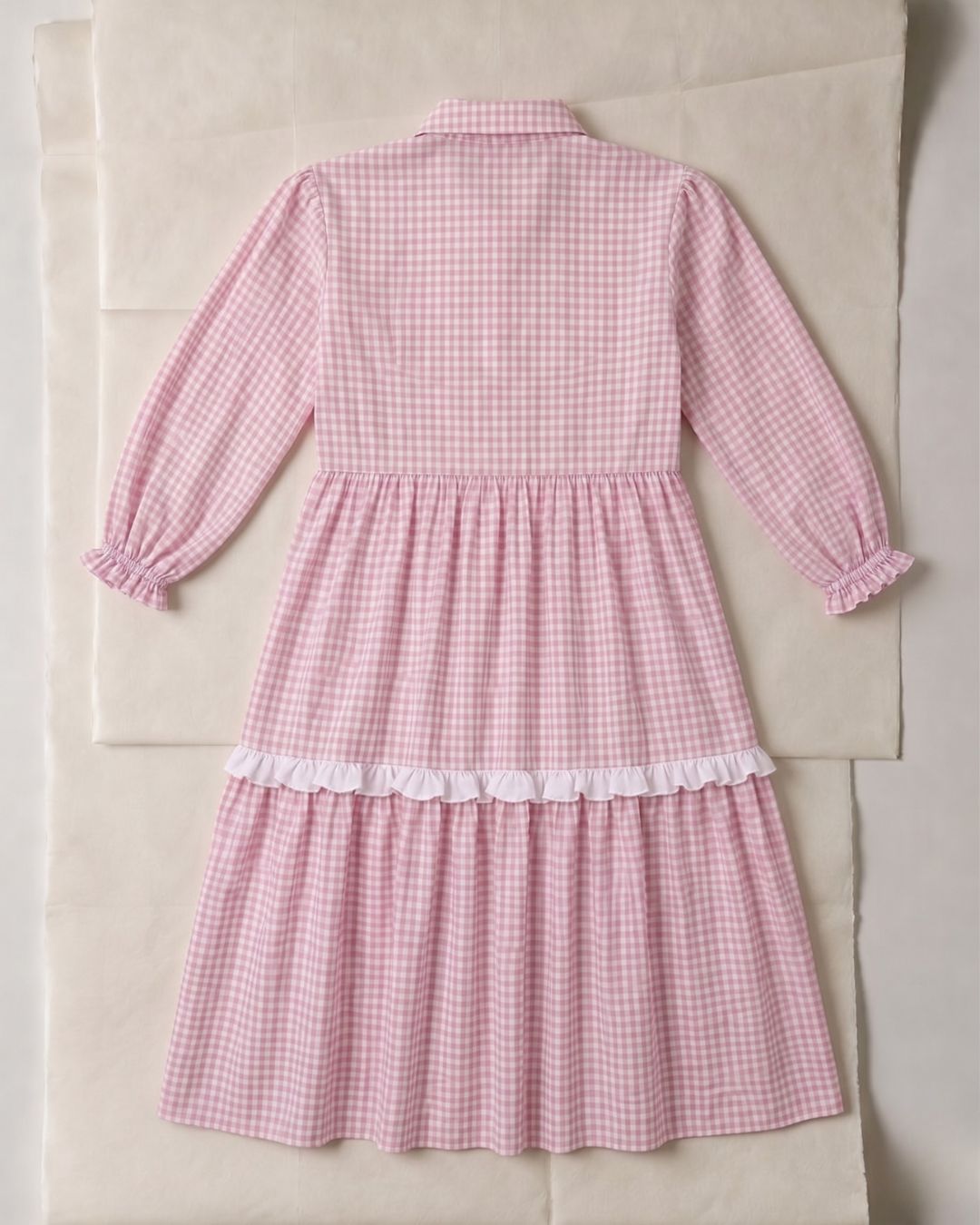 Pink gingham dress with white lace trim on a beige background