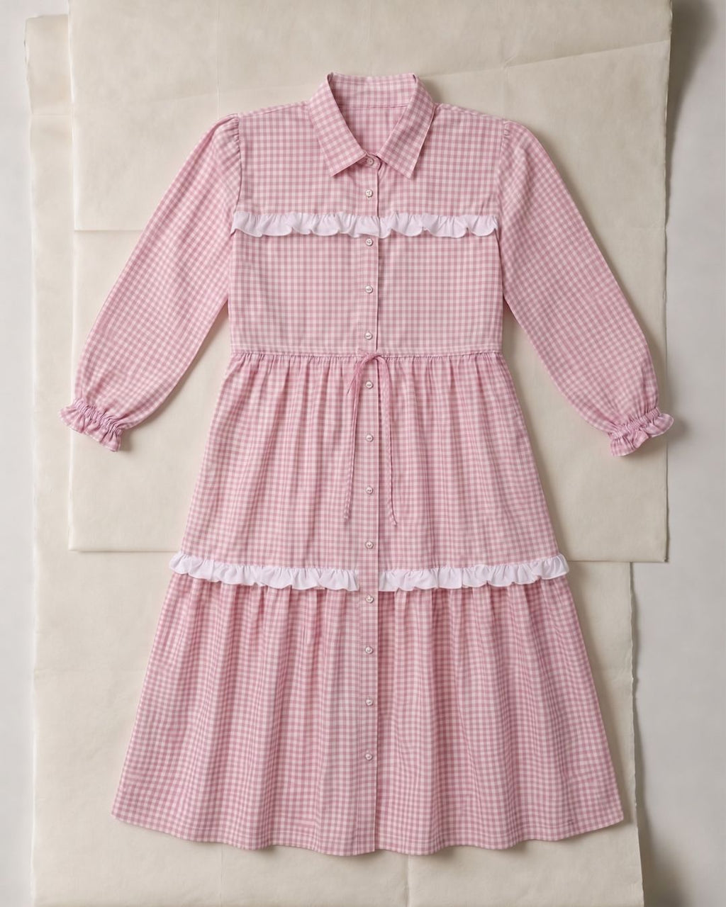 Pink gingham dress with white ruffles on a beige surface