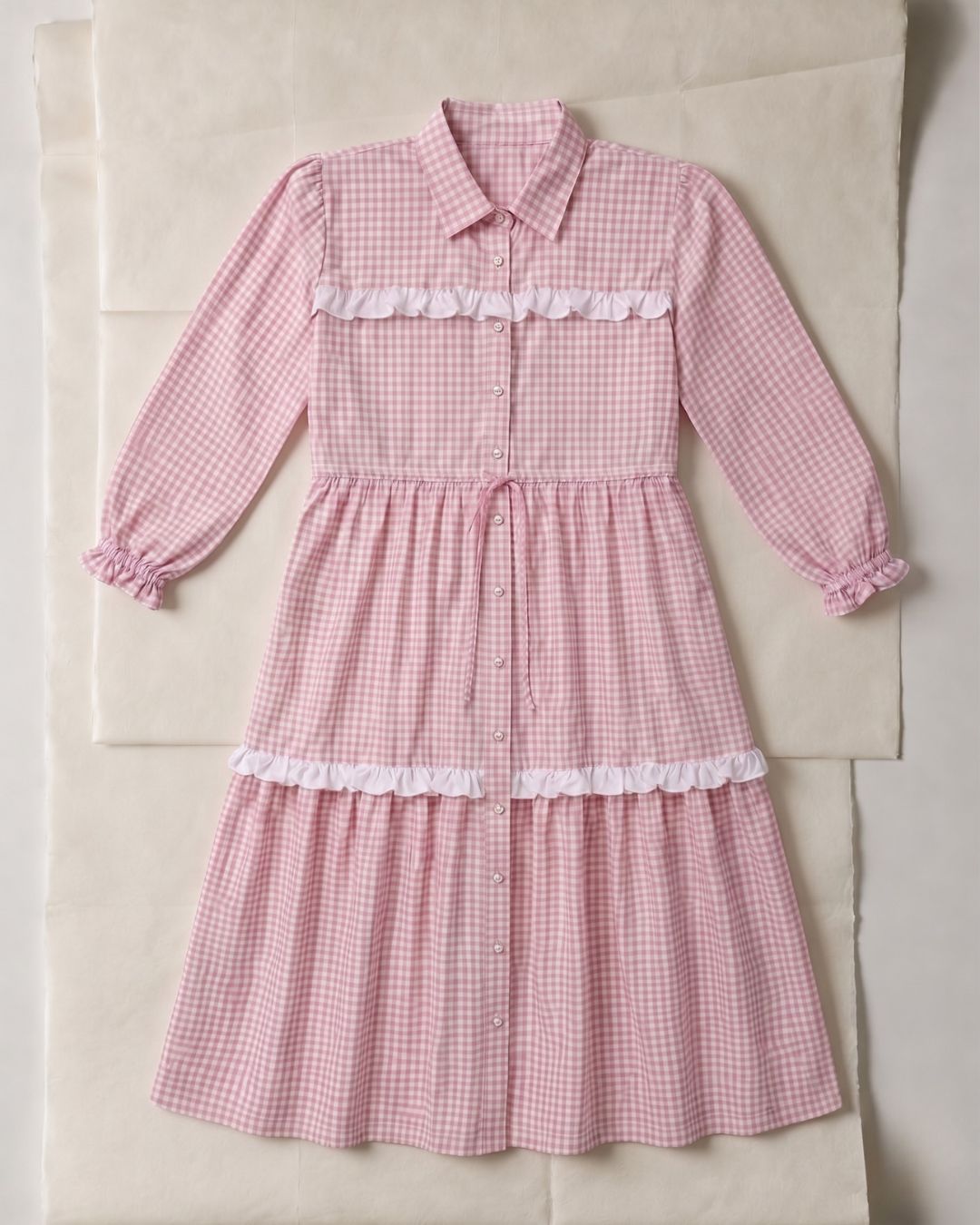Pink gingham dress with white ruffles on a beige surface